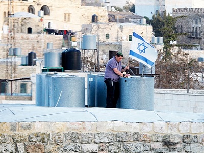 An Israeli settler puts an Israeli flag on the roof of a Palestinian house in a building in the center of the Palestinian city Hebron. (Photo: Via MEMO)